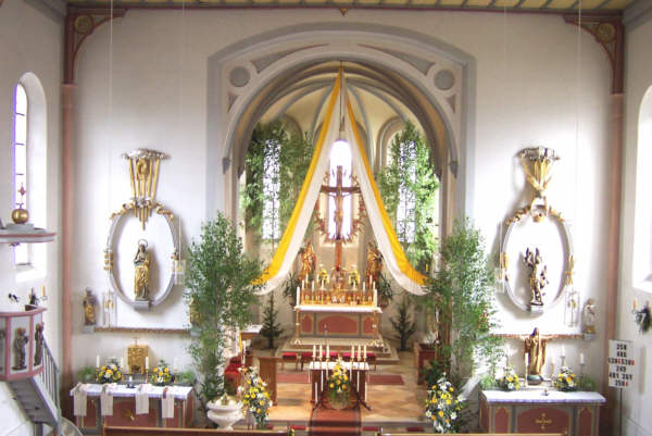Hofkirchen - Festlich geschmückt zum Priesterjubiläum 2003. Bemerkenswert ist das romanische Kreuz am Hochaltar. Dargestellt wird die Sterbeszene. Jesus lebt noch. Die Augen sind geöffnet. Die Seitenwunde fehlt.